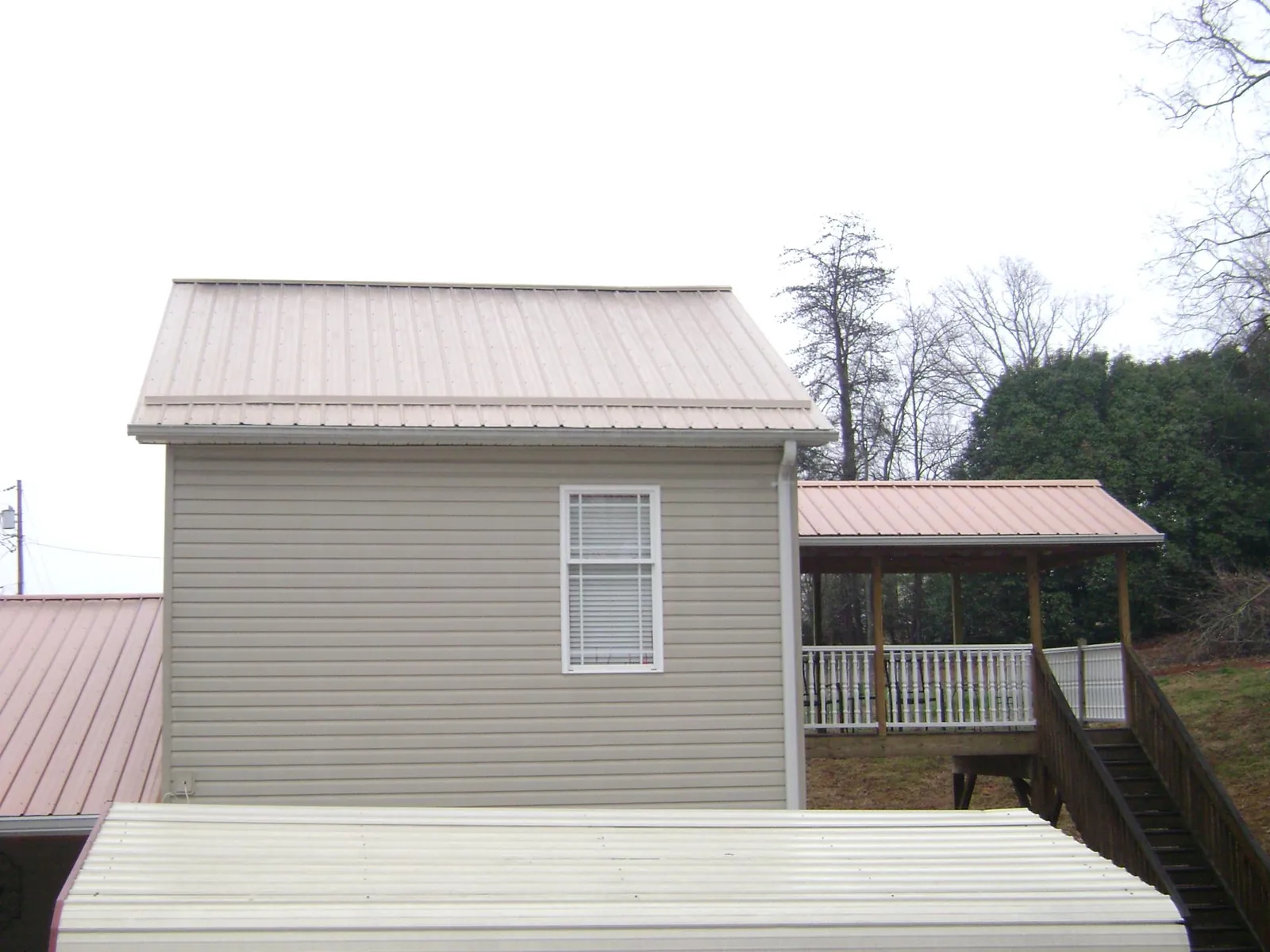 Tan metal roofs on a two story addition and attached porch, from a Roof Replacement job in Thompson